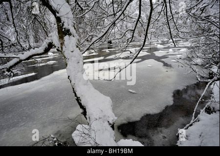 Snowy viale alberato di argini di fiumi e parzialmente Frozen River Foto Stock