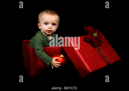 Stock di foto da un anno un bambino in una scatola avvolto in rosso, tenendo un ornamento di Natale. Foto Stock