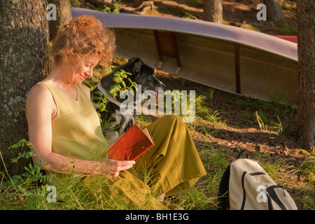 La donna si appoggia contro la struttura di libro di lettura, con il cane, Clear Lake, Equitazione Mountain National Park, Manitoba, Canada Foto Stock