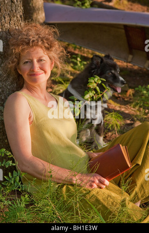 La donna si appoggia contro la struttura di libro di lettura, con il cane, Clear Lake, Equitazione Mountain National Park, Manitoba, Canada Foto Stock