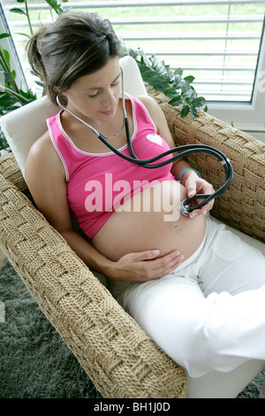 Donna incinta tenendo lo stetoscopio sulla pancia Foto Stock