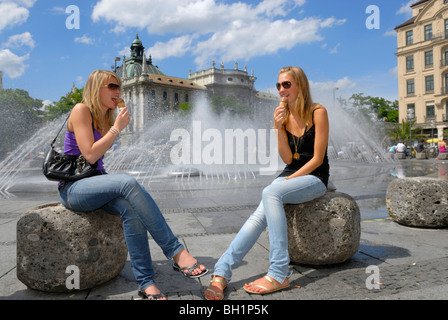 Due giovani donne a mangiare il gelato nella parte anteriore della fontana a Stachus, Karlsplatz, Monaco di Baviera, Baviera, Baviera, Germania Foto Stock