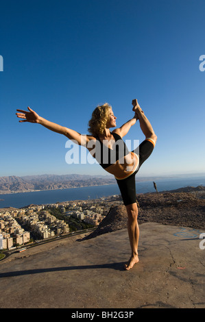 Giovane donna europea all'esterno esegue una serie di esercizi Yoga sullo sfondo della città di Eilat, Israele Foto Stock