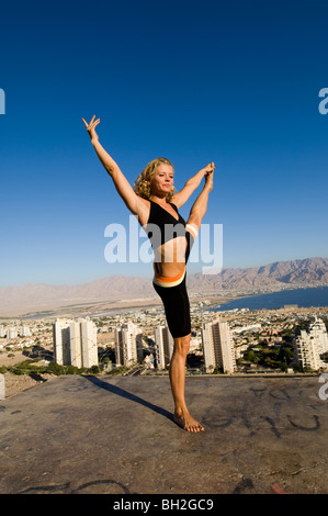 Giovane donna europea all'esterno esegue una serie di esercizi Yoga sullo sfondo della città di Eilat, Israele Foto Stock