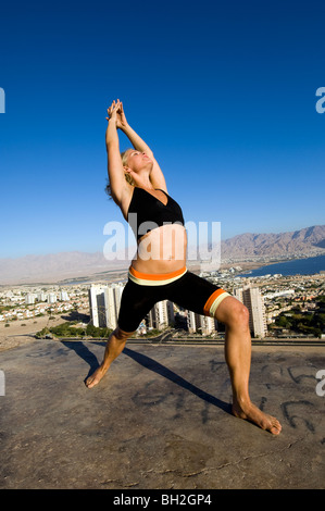 Giovane donna europea all'esterno esegue una serie di esercizi Yoga sullo sfondo della città di Eilat, Israele Foto Stock