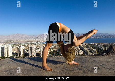 Giovane donna europea all'esterno esegue una serie di esercizi Yoga sullo sfondo della città di Eilat, Israele Foto Stock