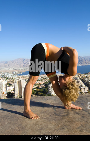 Giovane donna europea all'esterno esegue una serie di esercizi Yoga sullo sfondo della città di Eilat, Israele Foto Stock