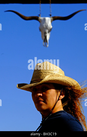 Una minoranza donna sondaggi lato del paese mentre in piedi di fronte ad un ambiente rustico in legno come gateway lavora come un proprietario terriero del bestiame Foto Stock