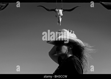 Una minoranza donna sondaggi lato del paese mentre in piedi di fronte ad un ambiente rustico in legno come gateway lavora come un proprietario terriero del bestiame Foto Stock