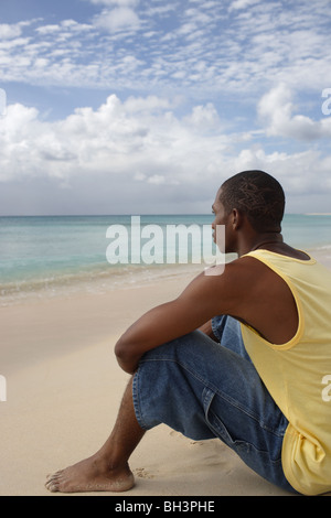 Giovane uomo seduto su una spiaggia tropicale che guarda verso il mare Foto Stock