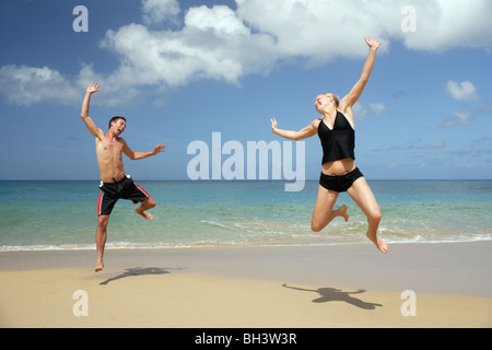 Coppia giovane saltando su una spiaggia tropicale, ridendo Foto Stock