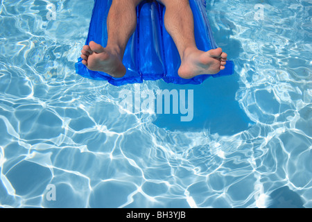Close up di un uomo per le gambe e i piedi rilassante su un gonfiabile lilo aria materasso galleggiante in una piscina con acqua blu Foto Stock