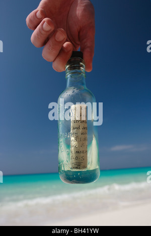 Un uomo con le mani in mano tenendo un messaggio in bottiglia su una deserta spiaggia tropicale Foto Stock