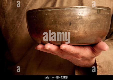 Il Tibetano Singing Bowl essendo trattenuto in alto nella parte anteriore del suono healing practitioner petto Foto Stock