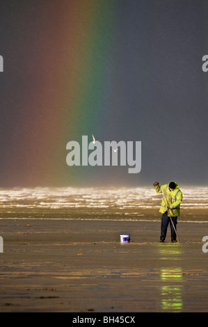 Il Cockle raccoglitrice in giacca gialla e rainbow in background su mare Foto Stock
