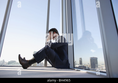 Un imprenditore seduto sul pavimento in un angolo di un ufficio grattacielo con la testa tra le mani