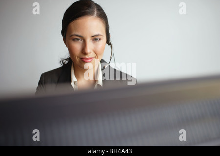 Giovane imprenditrice seduta a un computer di indossare una cuffia, sorridente Foto Stock