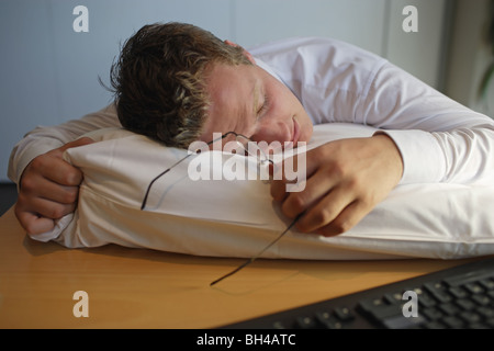 Giovane imprenditore addormentato su un cuscino sulla scrivania in ufficio Foto Stock