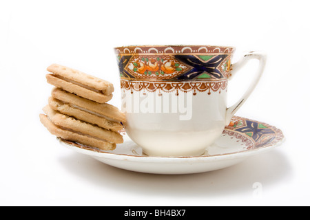 Tazza da caffè con piattino con pila di crema pasticcera biscotti isolata contro uno sfondo bianco. Foto Stock