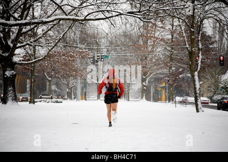 Un maschio di runner con uno zaino corre lungo una strada di città mentre indossano shorts in inverno. Foto Stock