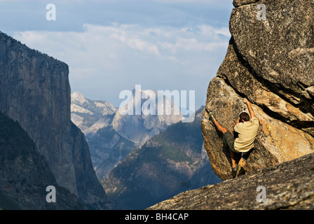 Con Half Dome e El Capitan in background, un giovane uomo è visto bouldering in Yosemite Valley, California. Foto Stock