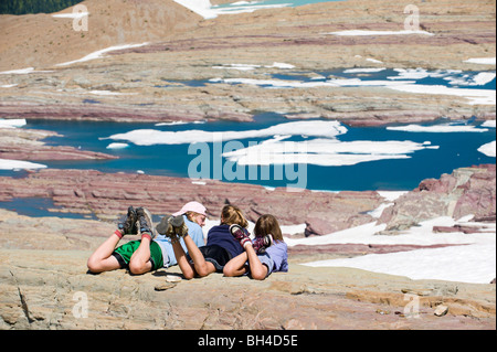 Tre giovani ragazze rilassatevi e godetevi il sole che si affaccia su un lago glaciale nel Parco Nazionale di Glacier, Montana. Foto Stock