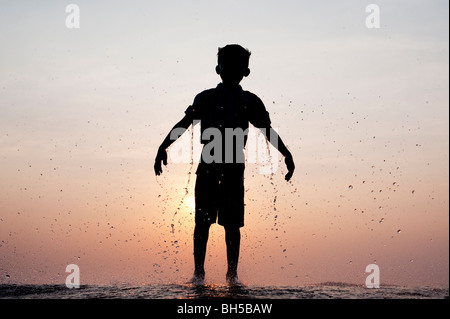 Ragazzo indiano gocciolante dopo aver acqua gettata su di lui contro un indiano al tramonto. Silhouette. Andhra Pradesh, India Foto Stock