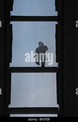 Un uomo che cammina attraverso il Millennium Bridge, fiume Thames, London, Regno Unito. Vista guardando attraverso il ponte in acciaio da sotto. Foto Stock