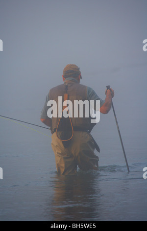 FLY FISHERMAN guadare in fiume con canna da mosca pesante velatura cattivo tempo Foto Stock