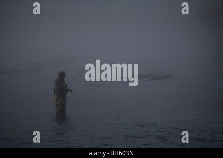 Pescatore a mosca la pesca in fiume con canna da mosca pesante velatura cattivo tempo Foto Stock