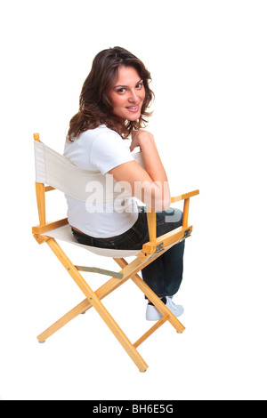 Una bruna donna in abbigliamento casual seduto su una poltrona regista guardando indietro sopra la sua spalla, isolato su uno sfondo bianco. Foto Stock