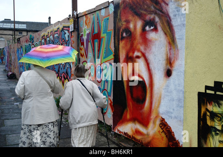 Due signore camminando sotto la pioggia passato graffiti di una testa della ragazza in Potterrow Edinburgh Foto Stock