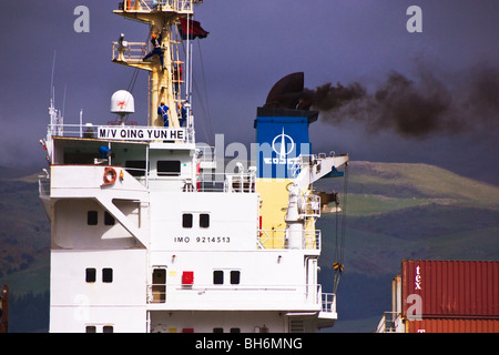 Una nave portacontainer emette fumo dall'imbuto durante ormeggiato a un terminale per container Foto Stock