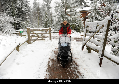 Giovane madre spingendo baby buggy in winter wonderland di neve England Regno Unito Foto Stock