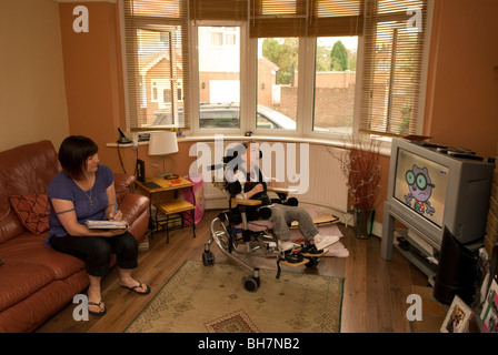 Donna che lavorano da casa con la figlia di disabili in background che soffre di paralisi cerebrale, Luton Regno Unito. (Modello rilasciato) Foto Stock