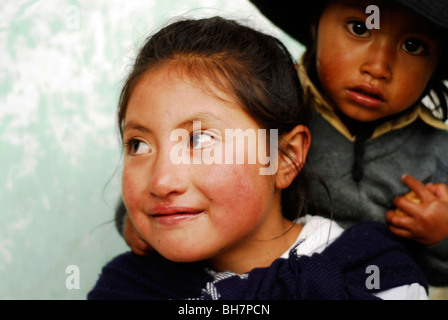 Ecuador, Latacunga, close-up di una ragazza ith la sua grande e luminosa occhi marroni e sorridente, le sue guance bruciata dal sole, w/ baby sorella Foto Stock