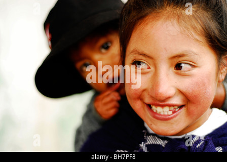 Ecuador, Latacunga, close-up di una ragazza ith la sua grande e luminosa occhi marroni e sorridente, le sue guance bruciata dal sole, w/ baby sorella Foto Stock