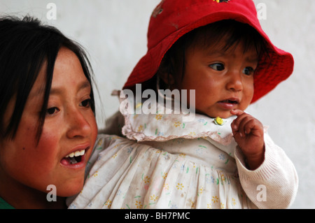 Ecuador, Latacunga, close-up di una ragazza che guarda lontano con il suo grande e luminosa occhi marroni, le sue guance bruciata dal sole, il suo bambino siblin Foto Stock