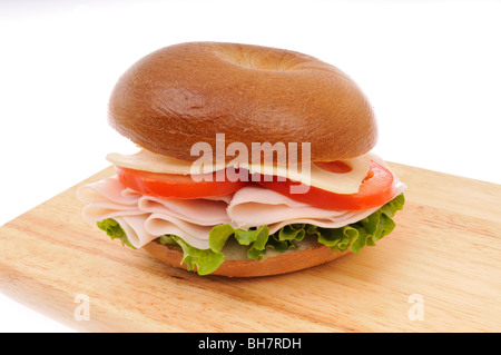 La Turchia, il formaggio svizzero e la lattuga e pomodoro bagel panino su un legno tagliere su sfondo bianco Foto Stock