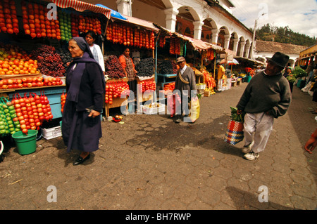 Ecuador, Otavalo, people shopping e passando da una strada fiancheggiata con coloratissime bancarelle di frutta e coloniale di edifici bianchi con ar Foto Stock