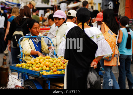 Ecuador, Otavalo, la vista di una donna scelta di frutti per un acquirente donna vestita di indigeni locali vestiti i suoi capelli intrecciati in una SAN Foto Stock