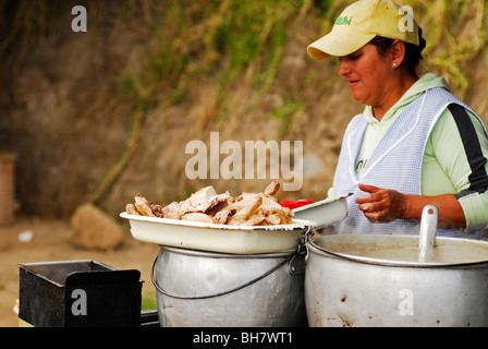 Ecuador, Otavalo, vista laterale di una donna con una luce blu grembiule a scacchi e un tappo giallo, cottura in una fase di stallo con profondo fritto c Foto Stock