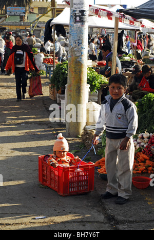 Ecuador, Saquisili, ragazzo giocando al traino di sua sorella bambino seduto in un rosso cassa in plastica Foto Stock