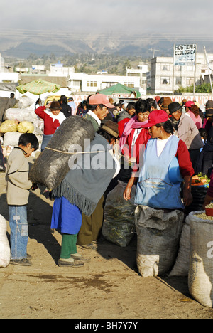 Ecuador, Saquisili, piccola vecchia persona che porta con sé un enorme sacco nero sulle sue spalle e la gente in background al mercato Foto Stock