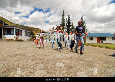 Ecuador, Yuarmachoa, alberi e case contro il cielo nuvoloso con basso angolo di visione dei bambini allegri in esecuzione in primo piano Foto Stock