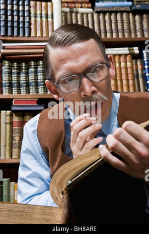 Un uomo che guarda scioccato durante la lettura di un libro in una libreria Foto Stock