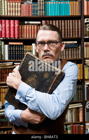 Un uomo con un libro in mano saldamente al suo petto e cercando di sospetto in una libreria Foto Stock