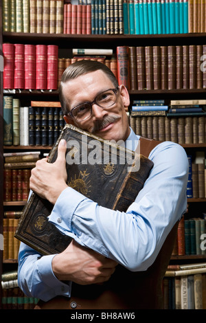 Un uomo con un libro in mano saldamente al suo petto felicemente in una libreria Foto Stock