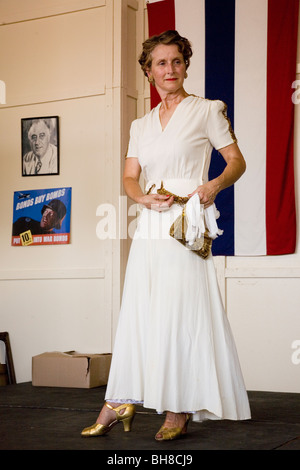 Donna attraente negli anni quaranta capi di abbigliamento in posa davanti alla bandiera durante una rievocazione storica di una guerra mondiale II sfilata di moda Foto Stock