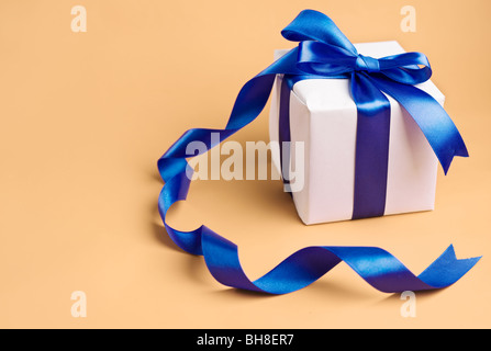 Dono del bianco con nastro blu su uno sfondo biege Foto Stock